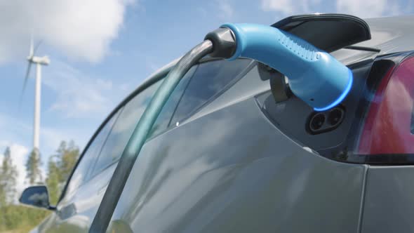 ZOOM OUT, GRAPHICS ENHANCED - A generic electric car charges in front of a wind turbine