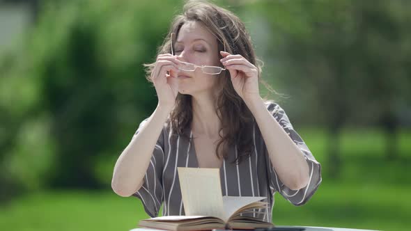 Middleaged Woman is Putting on Glasses to Read Book Outdoors Portrait of Charming Clever Lady