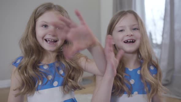 Positive Twin Sisters Waving and Sending Air Kisses To Camera, Caucasian Brunette Girls in Blue