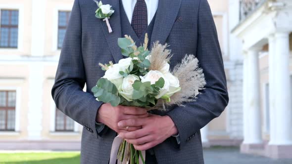 Close Up of Young Stylish Groom Hands Holding Beautiful White Wedding Bouquet