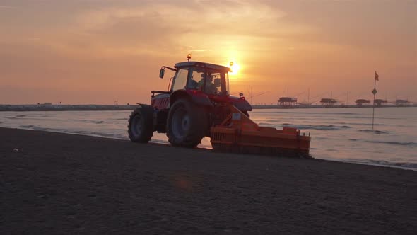 A tractor cleans the sand of the beach at sunrise