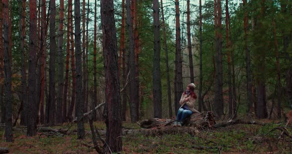 Nice Girl is Sitting on a Fallen Log in a Dense Forest She Looks at Nature and Dreams