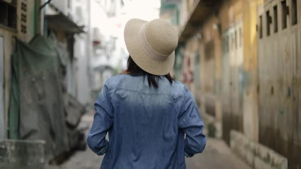 Portrait of young Asian woman traveler wearing retro fedora hat walking a small street in Bangkok.