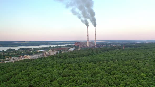 Aerial view on the green forest and pipes with smoke from plant.