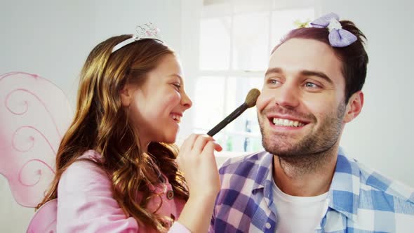 Girl dressed up in a fairy costume applying make-up on fathers face