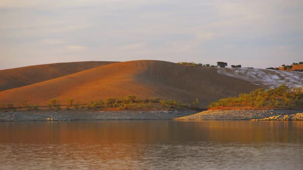 Desert like hill landscape with reflection on the water on a dam lake reservoir at sunset
