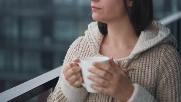 Woman Stays on Balcony During Snowfall with Cup of Hot Coffee or Tea