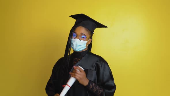 A Graduate Student in a Protective Mask Points with a Diploma in Hand Towards the Camera