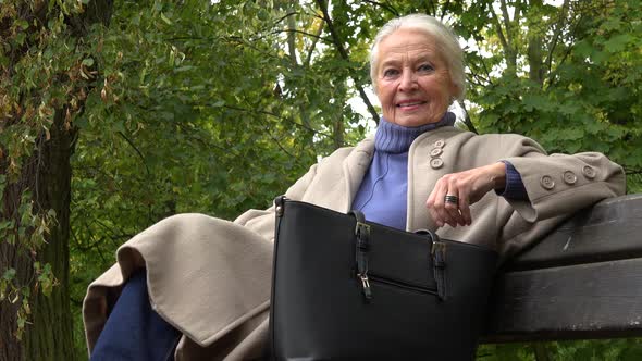 An Elderly Woman Sits on a Bench in a Park and Smiles at the Camera View From Below