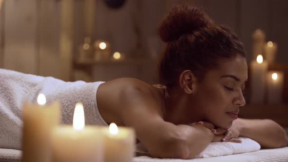 Beautiful Young African American Female Calmly Lying on Massage Table in Day Spa
