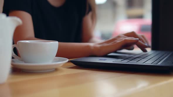 Closeup View of Woman's Hands Typing on the Laptop's Keyboard in the Coffee Shop During a Coffee