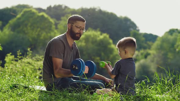 Father and Little Son Lifting Dumbbells Outdoors