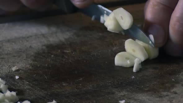 Close up of a mans fingers cutting garlic into pieces with a knife