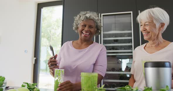 Happy senior diverse women drinking healthy drink in kitchen at retirement home