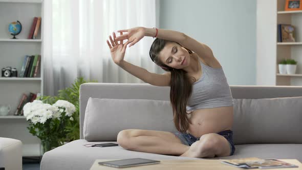 Future Mother Sitting on Couch in Headphones, Stretching Back, Audio Workout