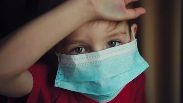 Young Boy in a Medical Mask Looks Out the Window. Self-isolation in Quarantine, Coronavirus, Covid