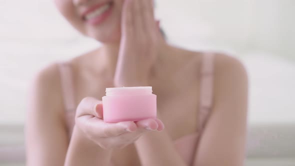 Closeup hand of young asian woman holding product cosmetic applying cream on facial.