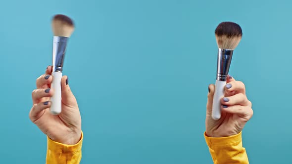 Female Hands Holding Face Makeup Brushes on Isolated Blue Background