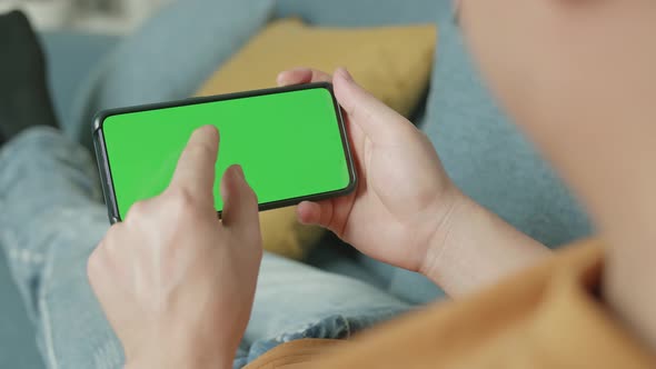 Male Using A Smartphone With Green Screen Display At Living Room While Lying On Sofa