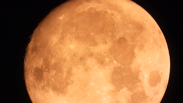 Extreme close-up shot of orange full moon in dark black sky; time lapse