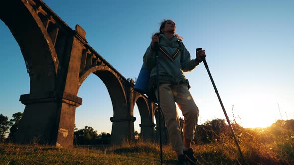 A Lady Is Doing Nordic Walking Near a Stone Bridge in Sunlight