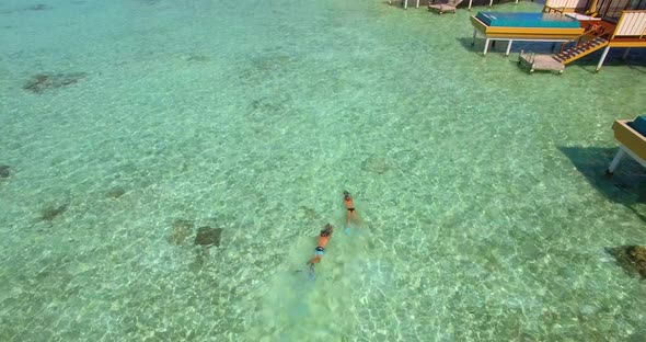 Aerial drone view of a man and woman couple with seascooters snorkeling near overwater bungalows