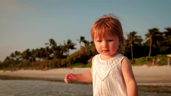 A Little Girl in a White Dress Stand Along the Beach