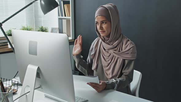 Muslim Woman Discussing Papers via Web Call on Computer