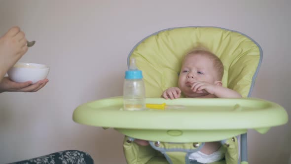 Mommy Feeds Little Son with Wholesome Meal in Highchair