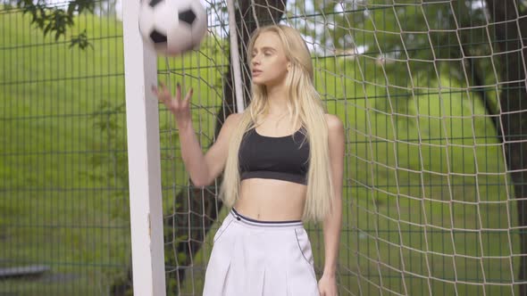 Portrait of Confident Beautiful Woman Posing with Ball at Soccer Net. Camera Approaches To Smiling