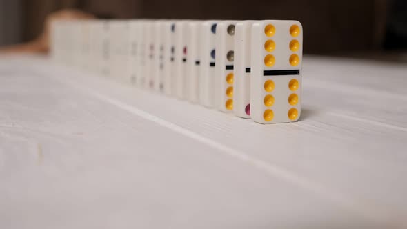 White Dominoes with Multicolored Dots Slowly Fall on a Light Wooden Background