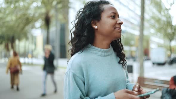 Pretty brunette African woman wearing blue sweater typing by phone and walking