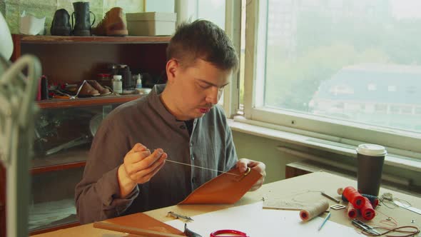 A Young Skilled Tailor Sews the Element To a Leather Bag Using a Tailor's Needle. In the Interior of