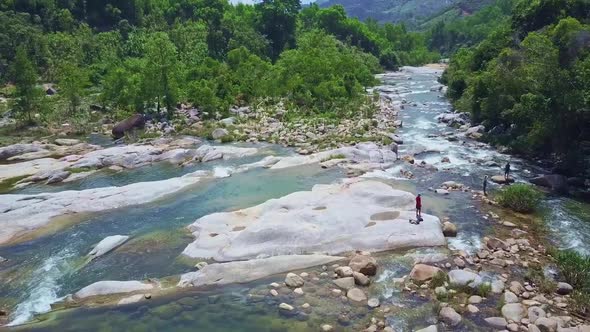 Drone Flies Over Rocky Bank River Tourists Stand on Stones