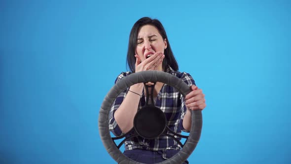 Portrait Sleepy Female Driver Yawns at the Wheel on a Blue Background Isolate