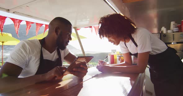African american couple wearing aprons using digital tablet and taking notes in the food truck