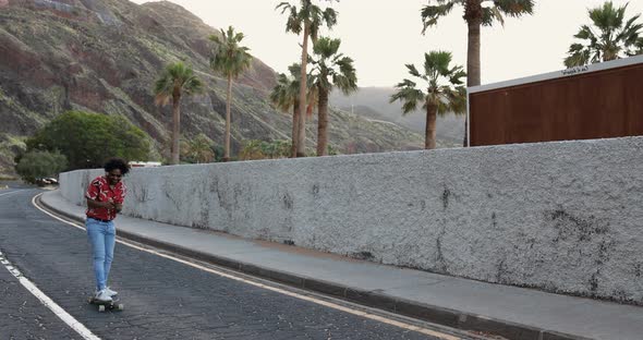 African american man riding a longboard on the road with palm trees in the background