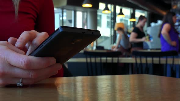 A Woman Sits at a Table in a Cafe and Works on a Smartphone - Closeup on the Phone