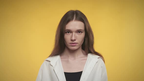 Young Adult Caucasian Woman is Looking at Camera on Bright Yellow Background