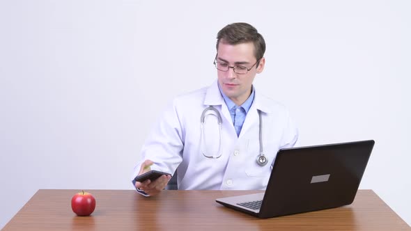 Young Happy Handsome Man Doctor Video Calling at Work Against Wooden Table