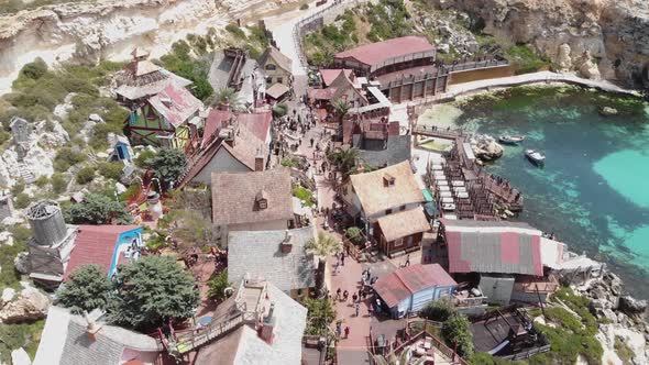 Aerial fly over shot of Popeye Village fun park Main Route full of tourists on Anchor Bay, in Malta