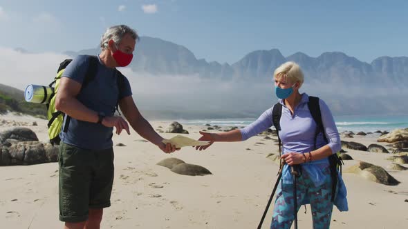 Senior hiker couple wearing face masks with backpacks and hiking poles reading maps while hiking