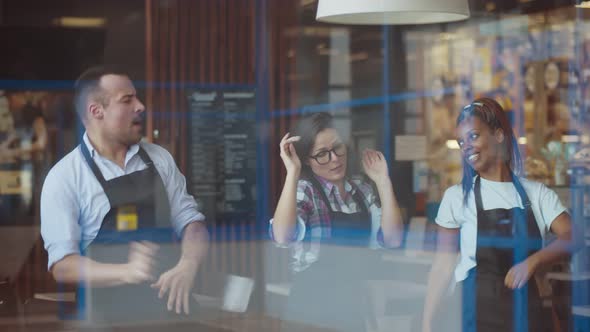 View Through Window of Cheerful Multiethnic Waiters Dancing Having Fun in Cafe