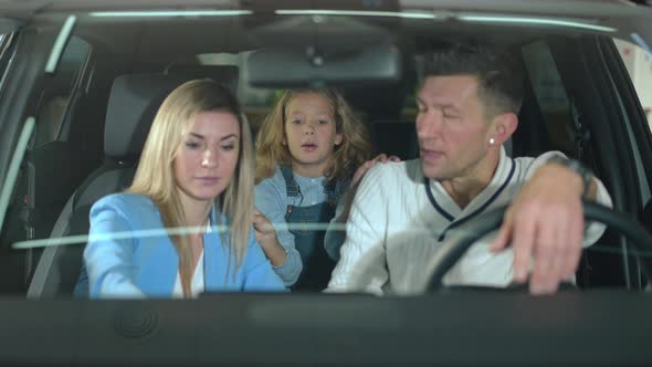 Shooting Through Windshield of Curios Cute Girl Talking to Man and Woman Sitting in New Car in