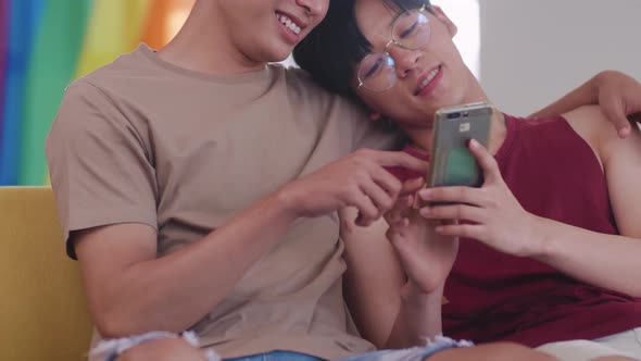 Happy gay Asian couple spending time together in living room at home.