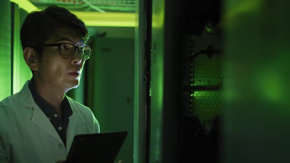 Asian male it technician in lab coat using tablet checking computer server