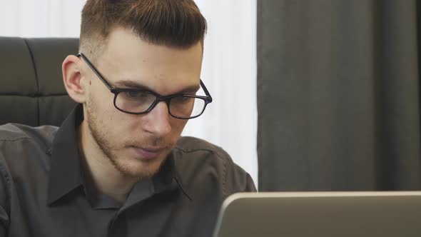 Young man in glasses looking at computer screen in the office. Business success concept