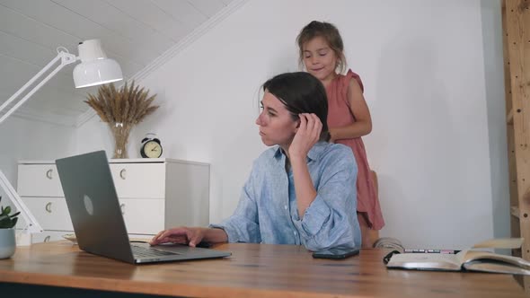 A Woman with a Child is Working at a Laptop