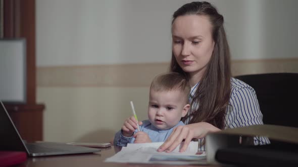 Busy Young Mother Working at Home with the Baby on Her Laps