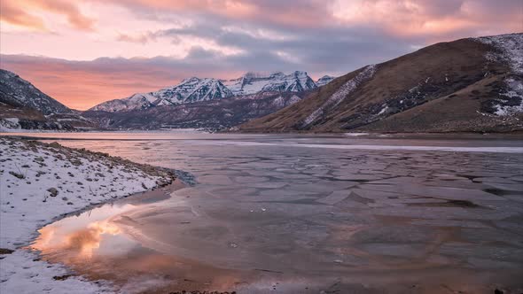 Time lapse over frozen lake looking at snow capped mountains during sunset